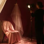 Photographe nu femme en studio clair-obscur, rideau ivoire et pose intimiste